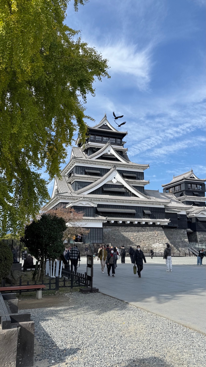 Kumamoto Castle under a blue sky with visitors in the foreground