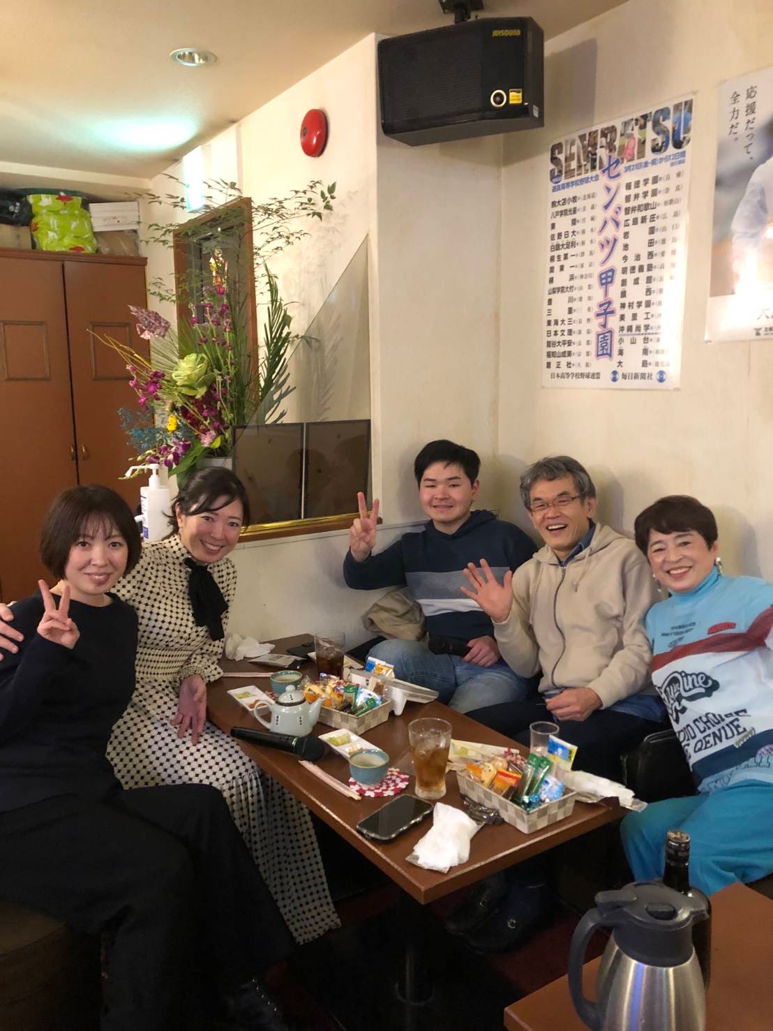 A group smiling around a table with drinks and a karaoke microphone inside the bar